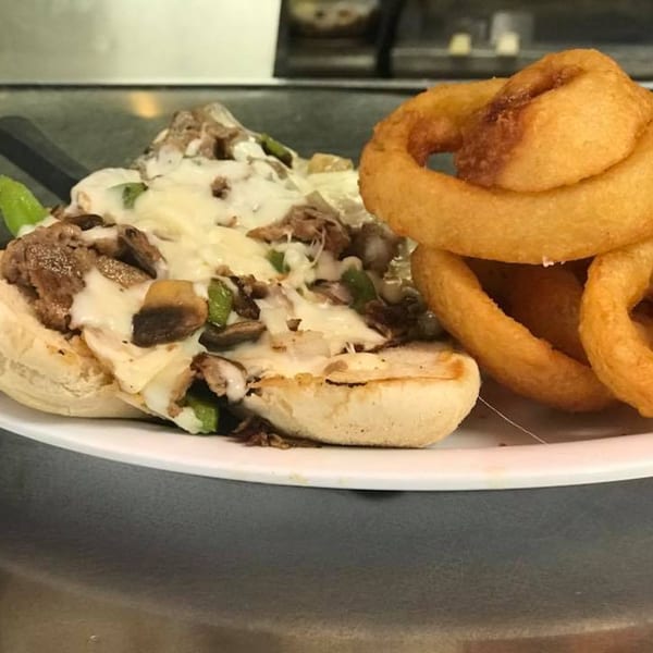 Cheesesteak sandwich with melted cheese, mushrooms, and green peppers, served with onion rings.