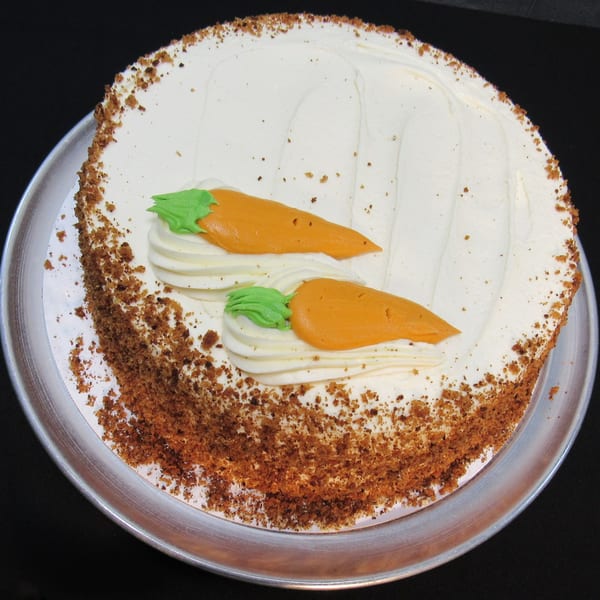 A whole carrot cake with white cream cheese frosting, topped with two orange icing carrots.
