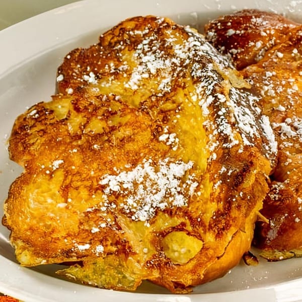 Golden-brown French toast dusted with powdered sugar on a white plate at Papa's New York Diner.