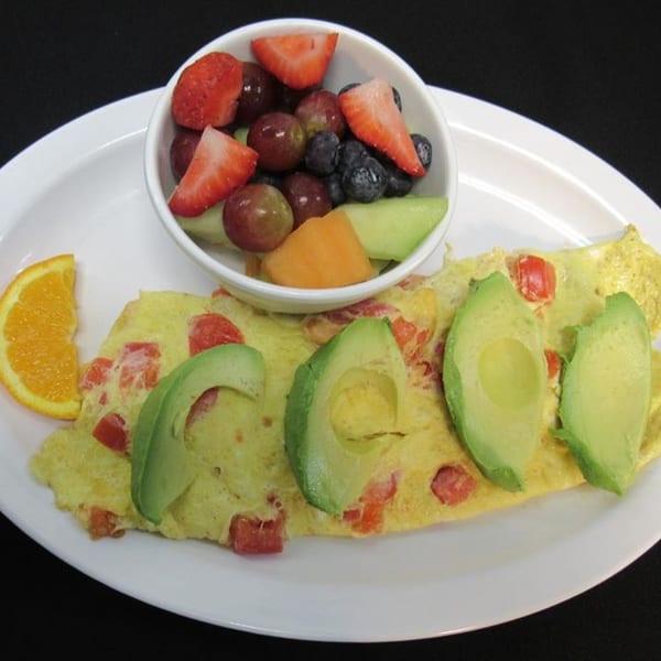 A Papa's New York Diner omelet with avocado and tomatoes, served with a fruit cup and orange slice.